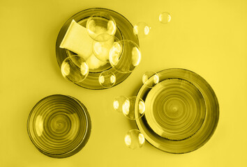 Abstract trendy yellow background with beautiful ceramic plates, cleaning sponge and soap bubbles. Washing dishes concept. Color 2021 concept. Flat lay style.