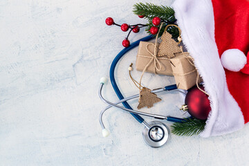 Stethoscope with branches of Christmas tree, Christmas gifts and red Christmas balls in Santa Claus hat on white concrete table. Concept Christmas and New year or Healthy New Year.Copy space.