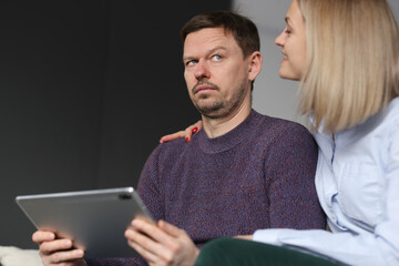 Pensive man sits with tablet next to smiling woman