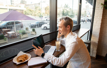 Young freelancer happy with a phone call. Remote work concept. Coffee house on background. Tasty...