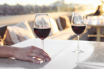 A man's hand holding a glass of red wine, sitting on a rooftop terrace, sunset light 