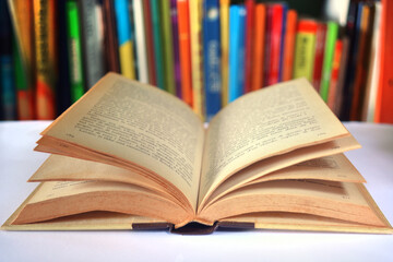 Close up of an open book and shelf with colorful books on background