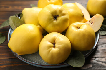Fresh ripe organic quinces with leaves on wooden table, closeup