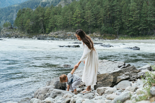 Young mother wearing white dress walking and enjoying  with little kid boy near mountain river outdoor