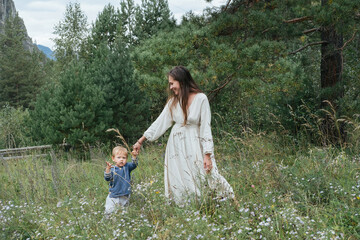 Naklejka na ściany i meble Young mother wearing white dress walking and enjoying with little kid boy in pine mountain forest