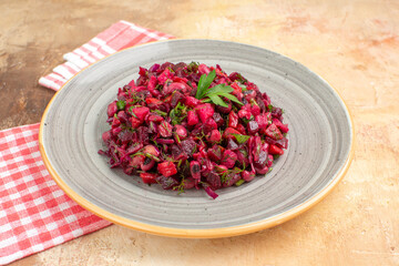 side close view of plate of a red salad with greens on it with checked napkin at the side on a wooden backgorund