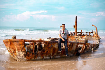Young man sits on the hull of an old ship. Looks at nature. The skeleton of an old destroyed ship...