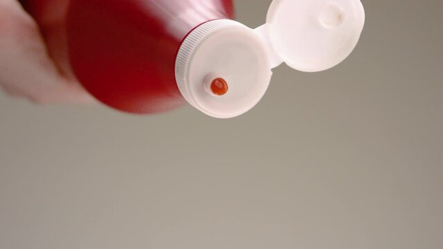 Ketchup being squeezed out of bottle. Stock footage. Close-up of jet of red ketchup on gray background. Ketchup spills out of large red bottle