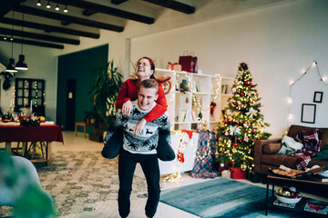 Loving man giving piggyback ride to woman in living room with garlands