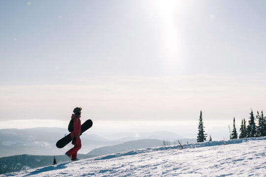 Female with snowboard. Snowboarder walking on snowy slop watching beautiful atmospheric mountain landscape