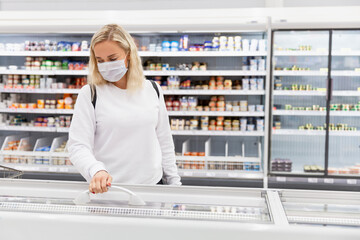 Young blond woman in mask at grocery store. Coronavirus pandemic.