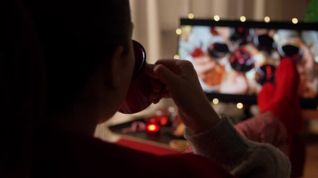 christmas, winter holidays and leisure concept - young woman watching movie on tv, drinking coffee or hot chocolate and resting feet in red knitted socks on table at cozy home