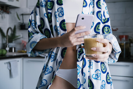 Beautiful young female wearing morning gown and white underwear shooting her smoothies on mobile phone