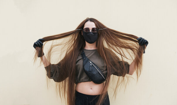 Young female wearing black face mask, latex gloves and sun glasses holding long hair with her hands