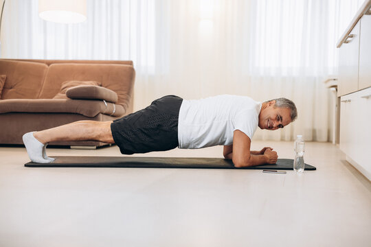 Plank It Confident Senior Man Doing Plank Position While Exercising On The Floor In Light Loft Interior. Hard Workout. Training At Home. Man Training To Have Fit Body. Morning Workout.