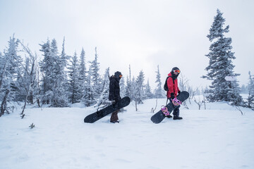 Young Female snowboarders walking in snowy spruce forest during snowfall winter day