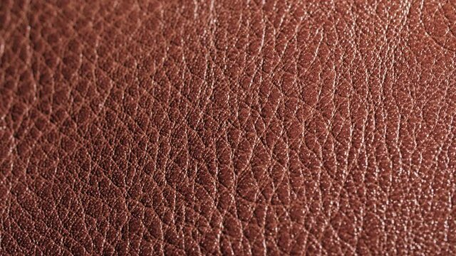 4K Rotating extreme close-up of real organic brown leather texture. Natural background pattern of animal skin used in fashion and clothing industry. Detail of shoe, purse, or other accessory.