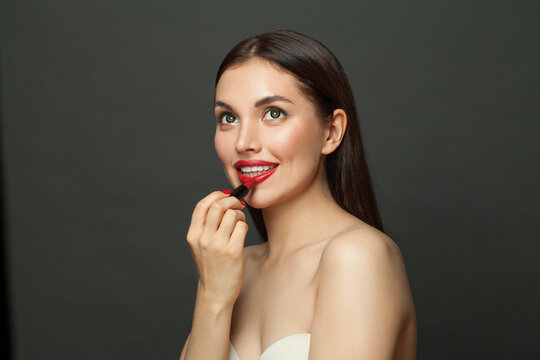 Attractive young woman applying lipstick makeup on lips on black background