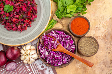 top view healthy beetroot salad on a gray ceramic plate with red onions garlic parsley bunch and a bowl of black pepper turmeric ground pepper red cabbage on a wooden table