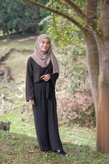 Beautiful and happy young moslem woman standing at the park in a sunny day with the green grass.