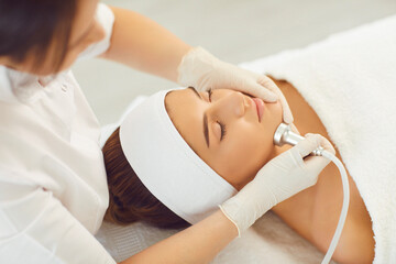 Cosmetologist making procedure of microdermabrasion of facial skin for woman
