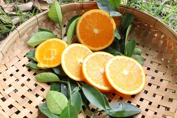 Orange fruit, fruits or vegetables with green leaves half and slices on wicker tray closeup.