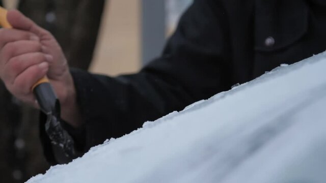 Person hand cleans electrocar windshield with rubber ice scraper of black and orange colours on cold day slow motion. Concept weather