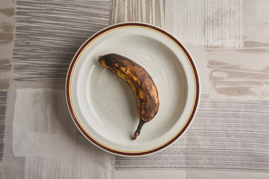 From above. Brown banana on a white plate.