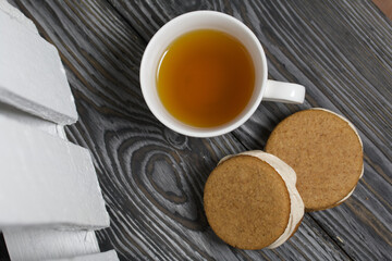 Gingerbread cookie with marshmallows. Marshmallow sandwich on black pine boards. Nearby is a cup of tea.