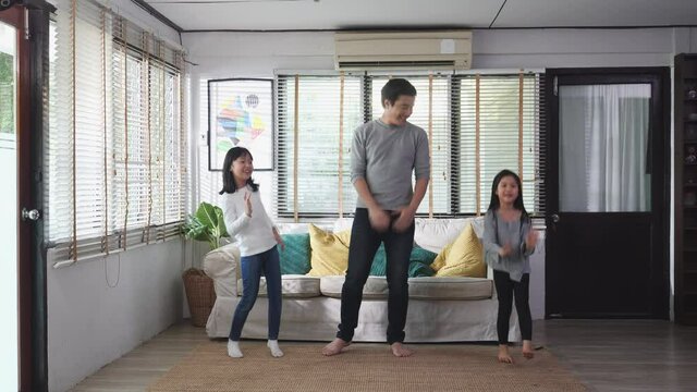 Asian family dancing together in living room at home. Father and daughter enjoyment with music while being celebration at home. Leisure activity stay at home of happy family.