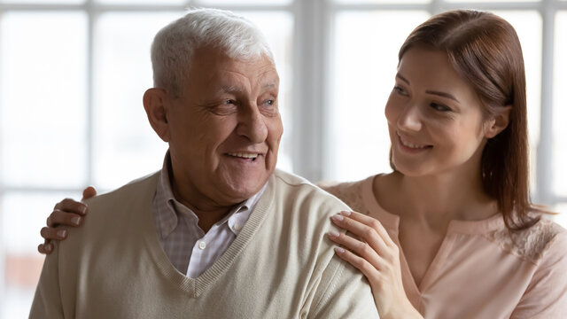 Attentive young lady caregiver social worker tender stroke shoulders of elderly man patient ask about needs propose help. Adult woman grownup child gentle touch mature father arms express support care