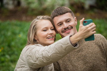 A young husband and wife take a selfie together on a smartphone for a blog on a social network on a green background. Close-up emotions