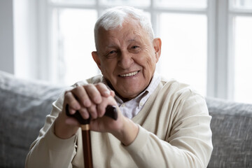 Portrait of happy senior grandfather sitting on couch looking at camera demonstrating white healthy...