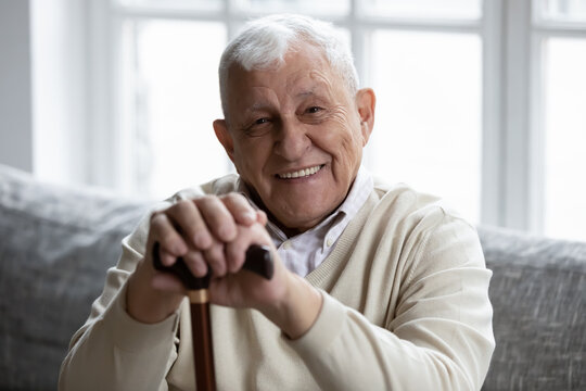Portrait of happy senior grandfather sitting on couch looking at camera demonstrating white healthy teeth in smile. Satisfied elderly man patient having healthy habit of regular visiting dental clinic