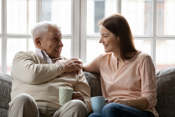 Happy smiling elderly father enjoy conversation with beloved grown daughter discuss news for cup of...