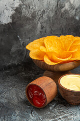 Front view of crispy potato chips decorated like flower shaped mayonnaise and ketchup on gray table