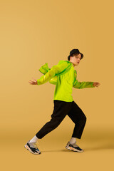 Fototapeta na wymiar Fire. Old-school fashioned young man dancing isolated on yellow studio background. Artist fashion, motion and action concept, youth culture, fashion returning. Young caucasian curly boy.