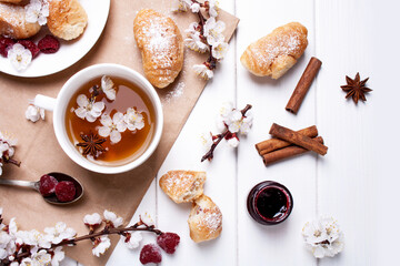Obraz na płótnie Canvas Cup of tea, croissants and spring flowering branches on a white wooden background. Flat lay style