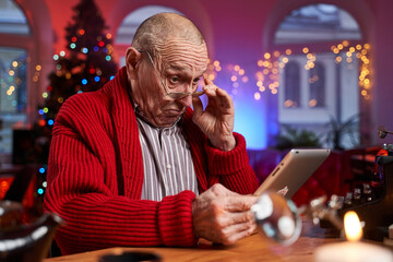 Portrait of an elder man with serious face dressed in red sweater with shirt weared with glasses poses in colourful room