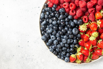 Fresh berries. Different berries in a white ceramic plate on a light table. Strawberries, raspberries and blueberries on a plate. Top view with space for text	