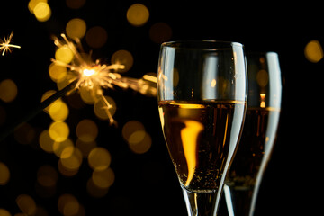 Two glasses of sparkling wine or champagne to celebrate New Year, Merry Christmas or Anniversary with a bokeh effect background. The yellow of the wine and lights stand out against a dark background.
