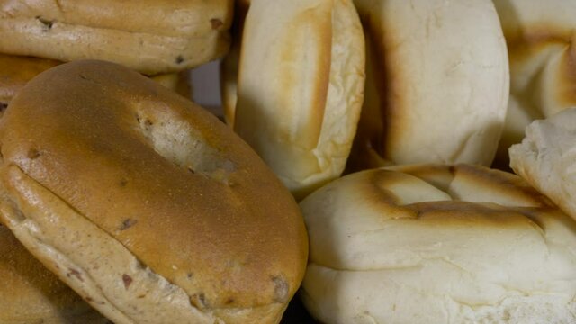 Closeup POV dolly shot of some fresh bread muffins and bagels, with a man&rsquo;s hand picking up a bagel at the end of the shot.