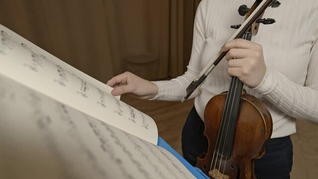 Female hand violinist flip through notes on music stand, background violin and bow. Gimbal shot of classical music notes in paper leaf through on a stand