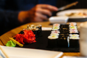 Tasty sushi rolls maki served on wooden cafe table. Close up shot of sushi and ginger with male hand on blur background. Selective focus