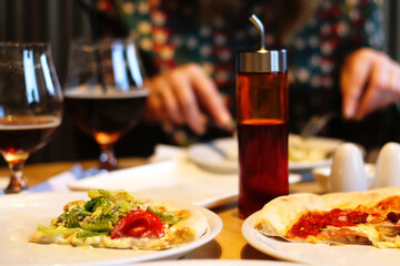 People eat pizza at a table in a cafe.A table in a cafe with pizza. Unfinished pizzas on a two plate. Glasses of beer, olive oil. Blur female hand on background. Selective focus