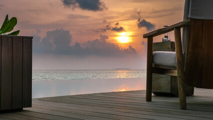 Fototapeta na wymiar Abenddämmerung mit Sonnenuntergang auf den Malediven im indischen Ozean, mit Lounge-Möbeln auf dem Pool-Deck und traumhafter Aussicht über den Pool aufs Meer