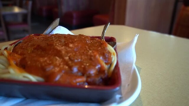 rotating 180 degree semi circle tabletop camera closeup of plated Italian spaghetti with red bolognese beefy sauce spiced herbed with a spoon and fork at a resturaunt with the background blurred