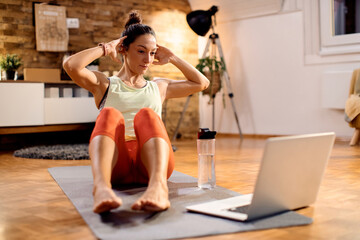 Athletic woman doing sit-ups during online training class at home.