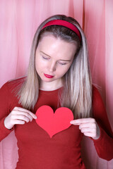 Young woman with blond hair is holding paper heart in her hands. Romantic photo for Valentine's Day