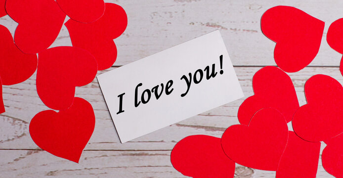 On a light wooden background, red hearts and a white card with the phrase I LOVE YOU in the center.